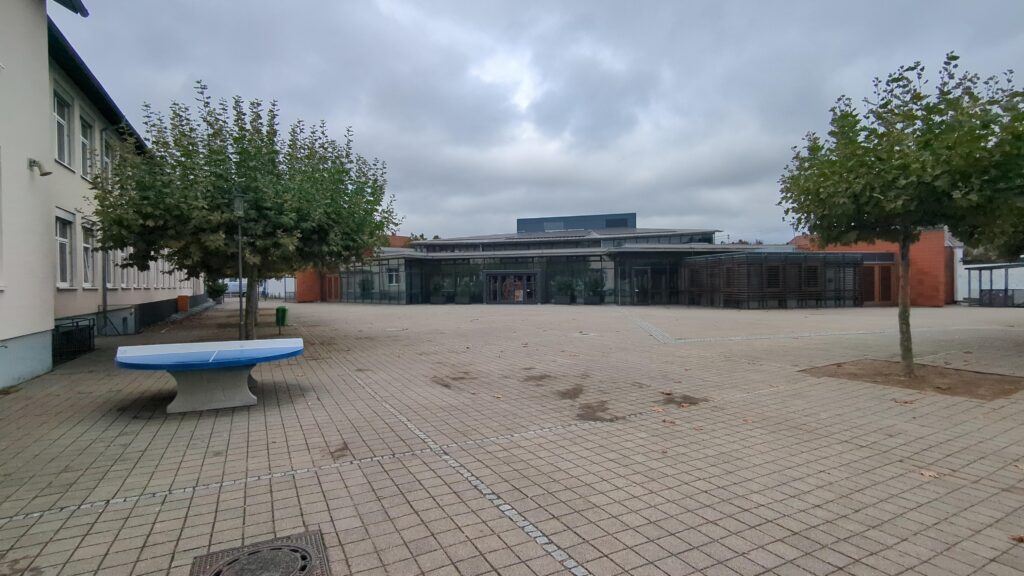 Ein großer zugepflasteter Platz. Drum Herum Gebäude und einzelne Bäume.